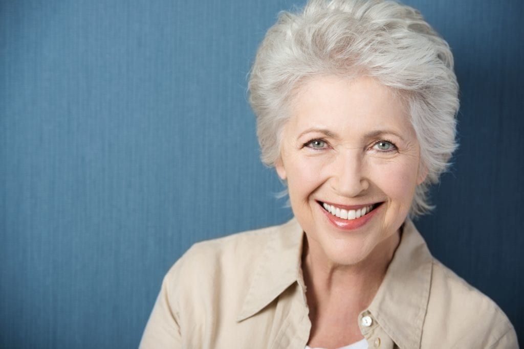 Senior woman smiling with beautiful teeth against a blue background